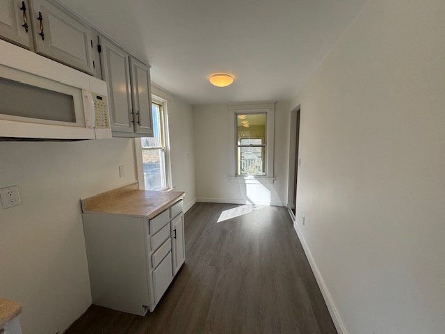 kitchen featuring light countertops, dark wood-style floors, white microwave, and baseboards