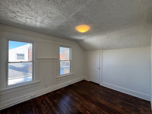 additional living space with vaulted ceiling, baseboards, dark wood-style flooring, and a textured ceiling