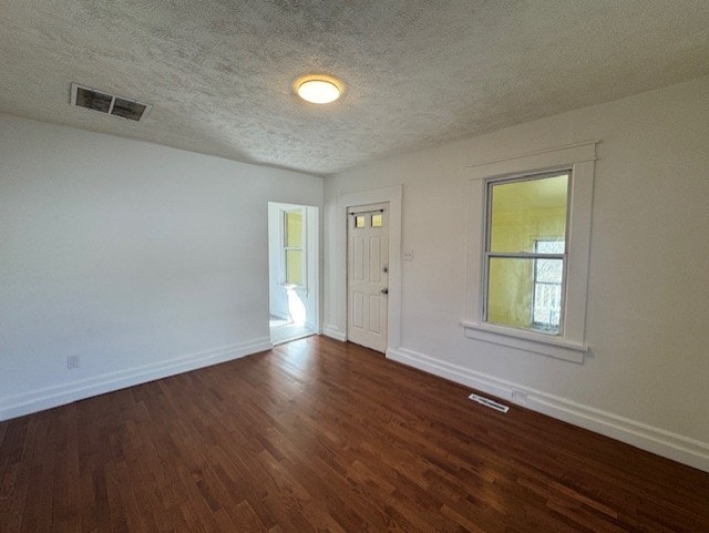 unfurnished room featuring dark wood-style floors, visible vents, a textured ceiling, and baseboards