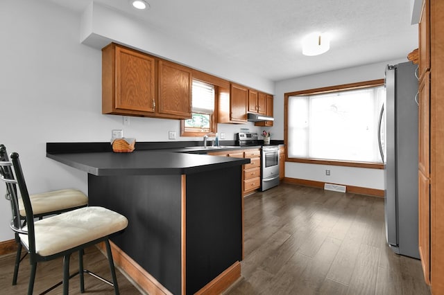 kitchen featuring visible vents, a breakfast bar, a peninsula, stainless steel appliances, and dark countertops