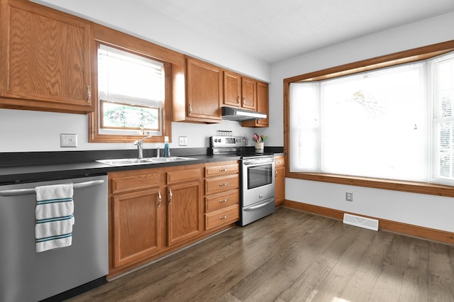 kitchen with dark countertops, visible vents, under cabinet range hood, appliances with stainless steel finishes, and a sink