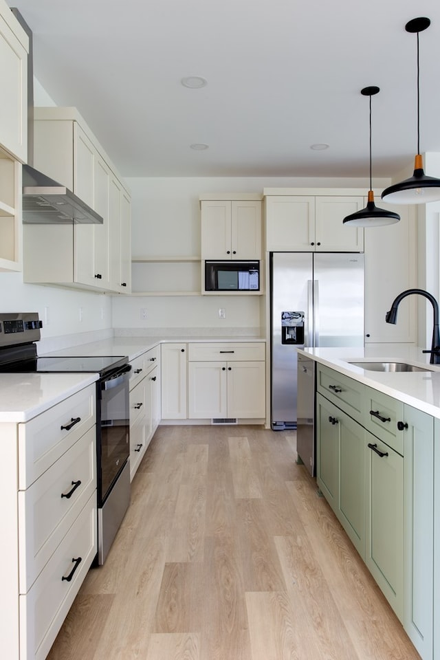 kitchen featuring sink, green cabinets, built in appliances, decorative light fixtures, and light wood-type flooring