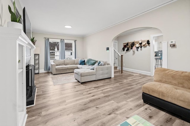 living room featuring stairway, arched walkways, ornamental molding, and light wood-style flooring