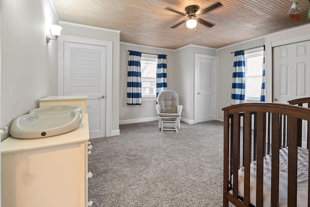 carpeted bedroom featuring ornamental molding, wooden ceiling, baseboards, and two closets