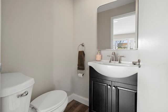 half bath with wood finished floors, vanity, toilet, and baseboards