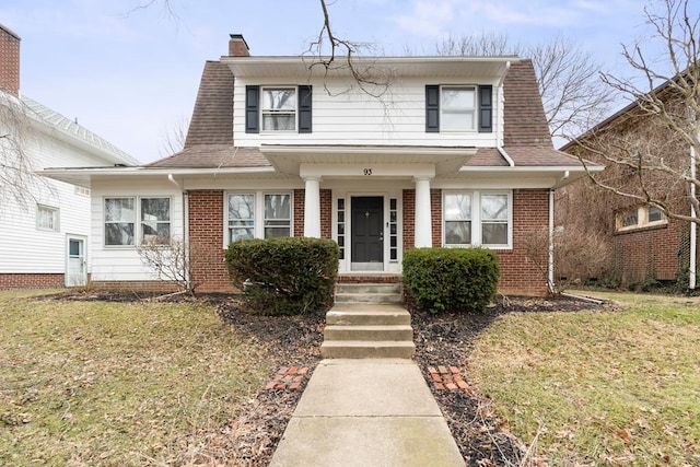 dutch colonial featuring brick siding, roof with shingles, a chimney, and a front yard