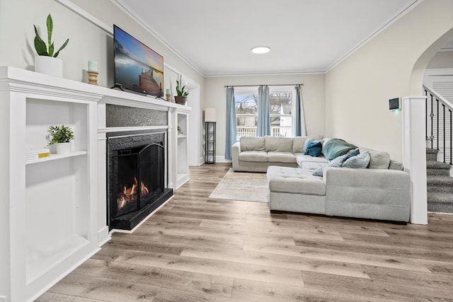 living room featuring light wood-style floors, a lit fireplace, stairway, and ornamental molding