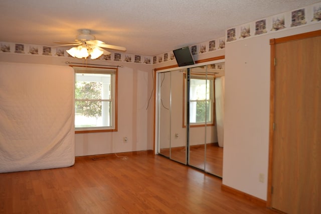 unfurnished bedroom with multiple windows, ceiling fan, wood-type flooring, and a textured ceiling