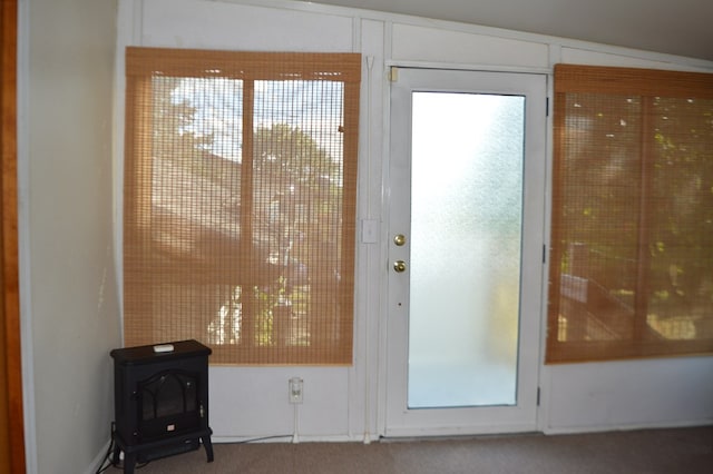 doorway to outside featuring carpet, a wood stove, plenty of natural light, and lofted ceiling