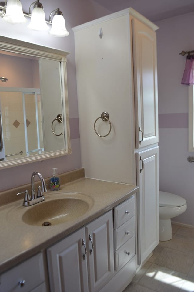 bathroom featuring toilet, vanity, tile patterned floors, and walk in shower