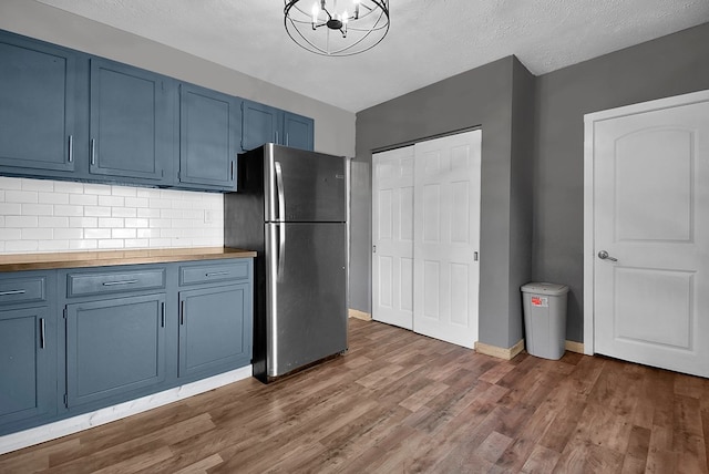 kitchen with wooden counters, blue cabinetry, dark wood-style flooring, and freestanding refrigerator