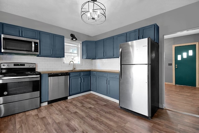 kitchen with appliances with stainless steel finishes, blue cabinets, wooden counters, and backsplash