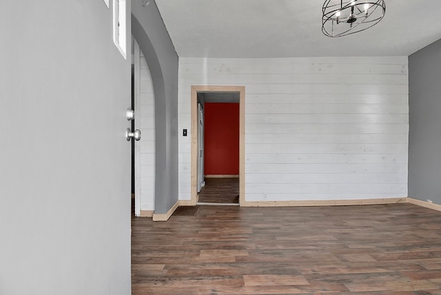 spare room with arched walkways, baseboards, and wood finished floors