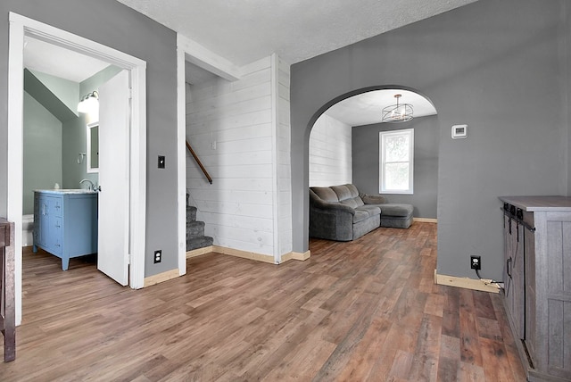 unfurnished living room with arched walkways, stairway, baseboards, and wood finished floors