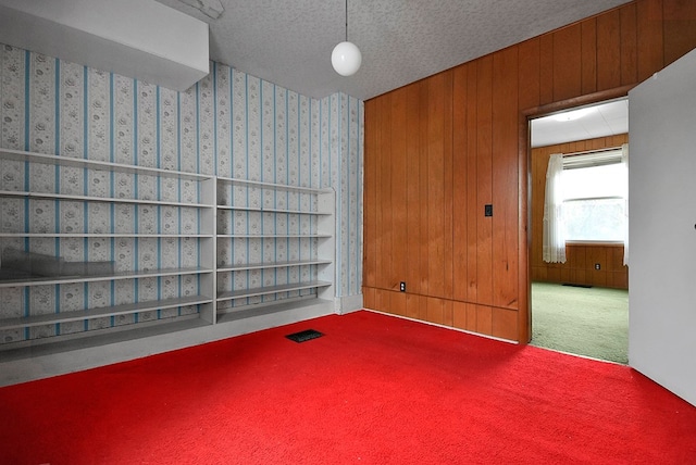 empty room featuring carpet flooring, wood walls, and a textured ceiling