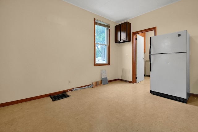 kitchen featuring white refrigerator, dark brown cabinetry, and light carpet