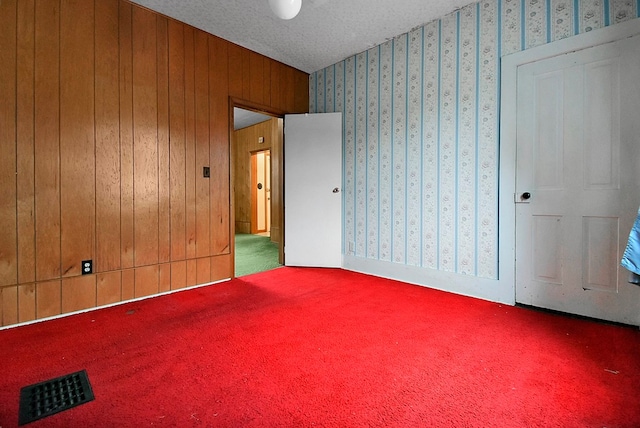 carpeted empty room with a textured ceiling and wood walls