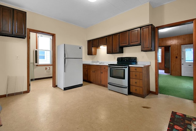 kitchen with stainless steel electric stove, white fridge, dark brown cabinetry, and wooden walls