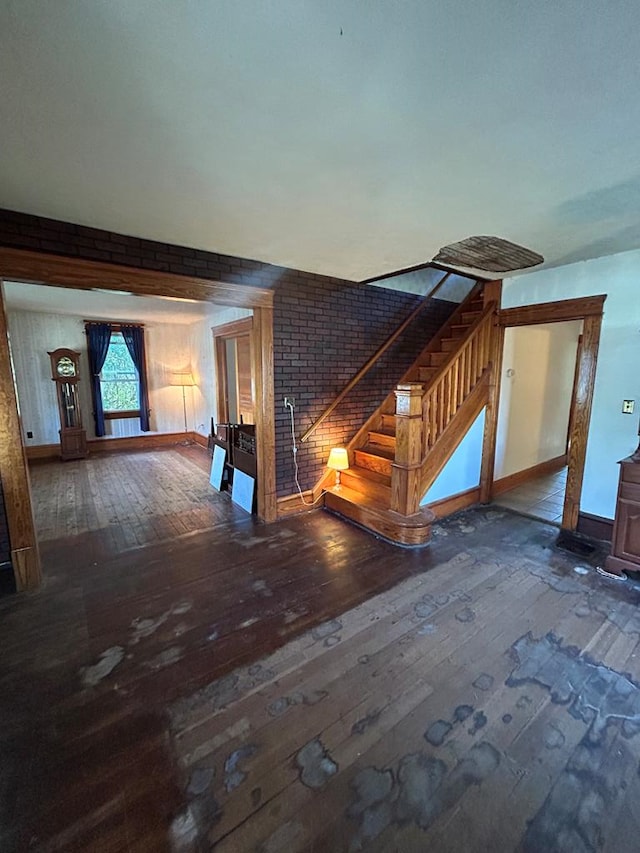 1221 N Sandusky Ave, Bucyrus, OH 44820 - unfurnished living room featuring hardwood / wood-style floors, stairway, and brick wall
