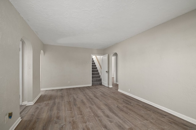 unfurnished room with baseboards, stairs, wood finished floors, arched walkways, and a textured ceiling