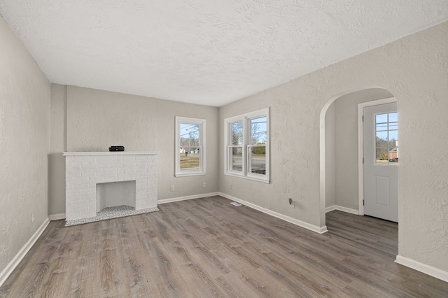 unfurnished living room with arched walkways, wood finished floors, and a textured wall