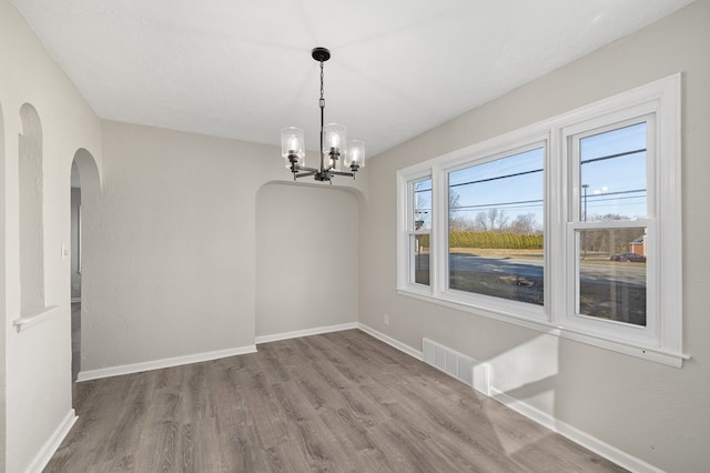 unfurnished dining area with arched walkways, visible vents, baseboards, and wood finished floors