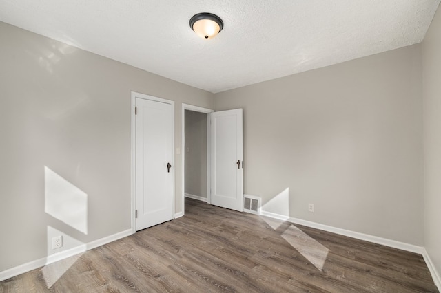 unfurnished room with a textured ceiling, wood finished floors, visible vents, and baseboards