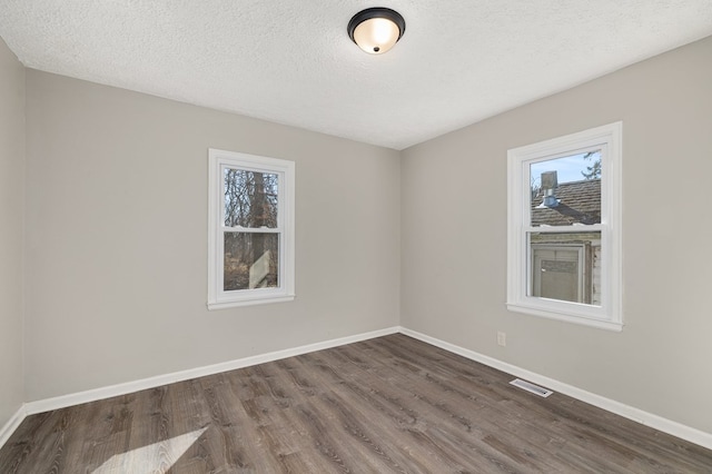 empty room featuring dark wood-style floors, a healthy amount of sunlight, and baseboards