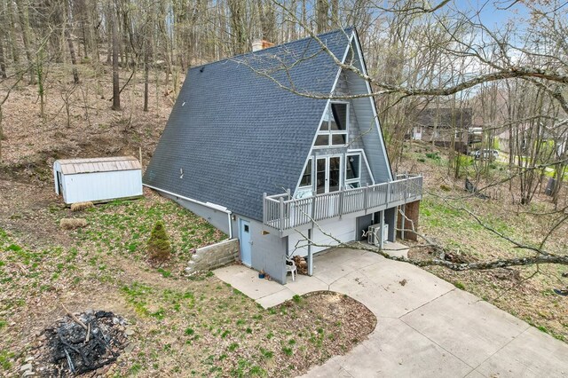 view of side of property featuring a storage shed, roof with shingles, driveway, a chimney, and a garage