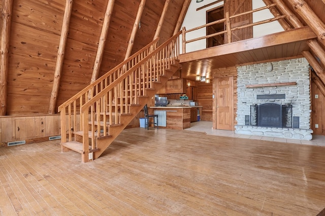 unfurnished living room featuring light wood-style flooring, beam ceiling, wood ceiling, wooden walls, and high vaulted ceiling