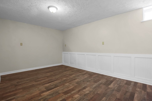 spare room featuring dark wood finished floors, a textured ceiling, and a wainscoted wall