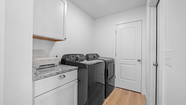 clothes washing area with light wood-style flooring, washing machine and dryer, and cabinet space