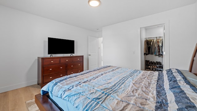 bedroom with light wood-type flooring, a closet, a walk in closet, and baseboards