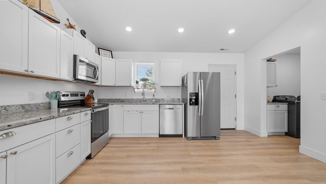 kitchen featuring appliances with stainless steel finishes, washer / clothes dryer, white cabinets, and light stone countertops