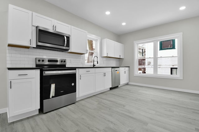 kitchen featuring sink, stainless steel appliances, white cabinets, decorative backsplash, and light wood-type flooring