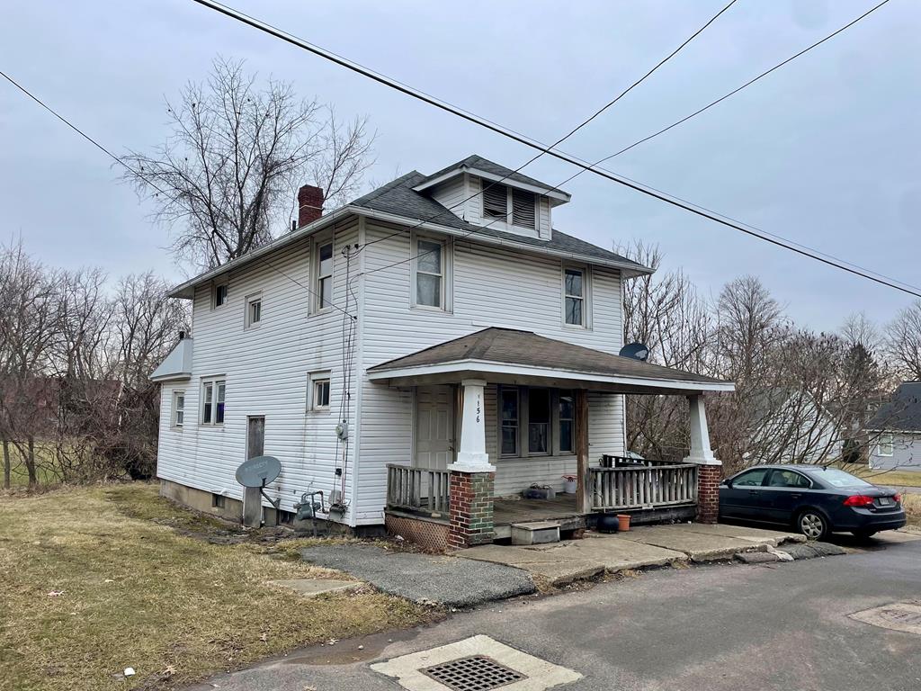 american foursquare style home featuring covered porch, a chimney, and a front yard