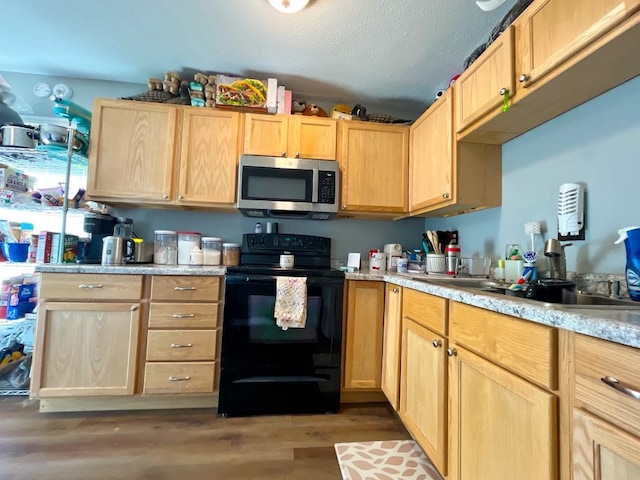 kitchen with light brown cabinets, stainless steel microwave, black range with electric cooktop, light wood-style floors, and light countertops