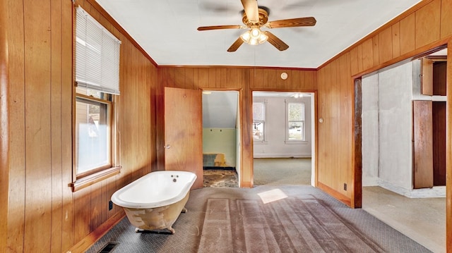 bathroom featuring ornamental molding, ceiling fan, a tub, and wood walls