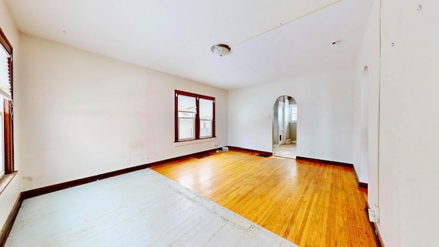 unfurnished room with arched walkways, wood finished floors, and baseboards