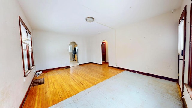 empty room featuring arched walkways, visible vents, light wood-style flooring, and baseboards