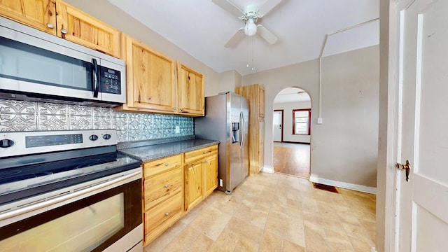 kitchen with arched walkways, ceiling fan, stainless steel appliances, tasteful backsplash, and dark countertops