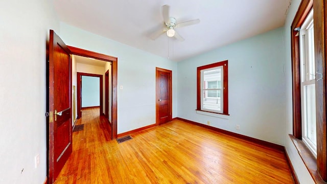 unfurnished bedroom with light wood-style flooring, a ceiling fan, visible vents, and baseboards