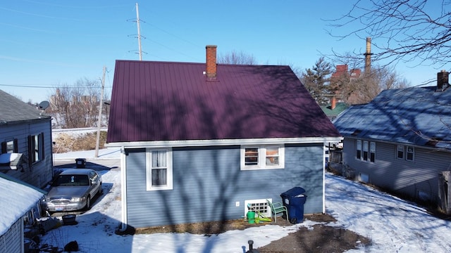 snow covered back of property with a chimney and metal roof