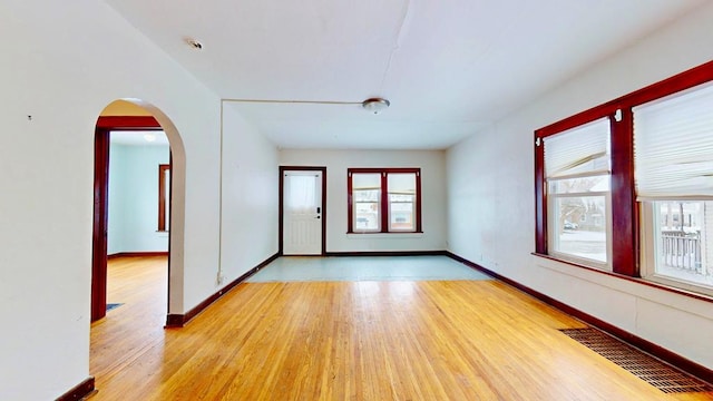 empty room with arched walkways, a wealth of natural light, light wood finished floors, and visible vents