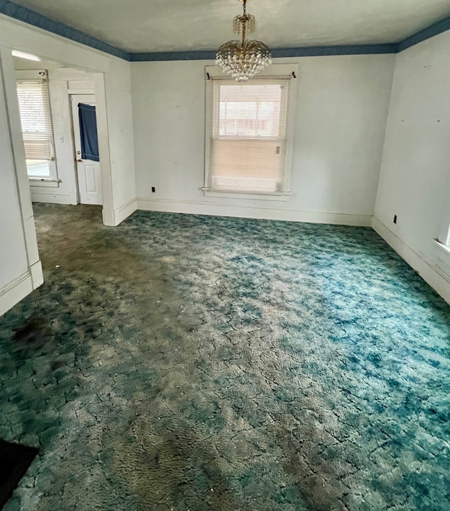 spare room with a chandelier, dark colored carpet, ornamental molding, and baseboards