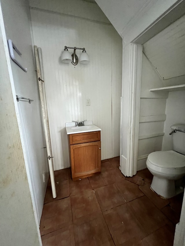 bathroom with toilet, vanity, vaulted ceiling, and tile patterned floors