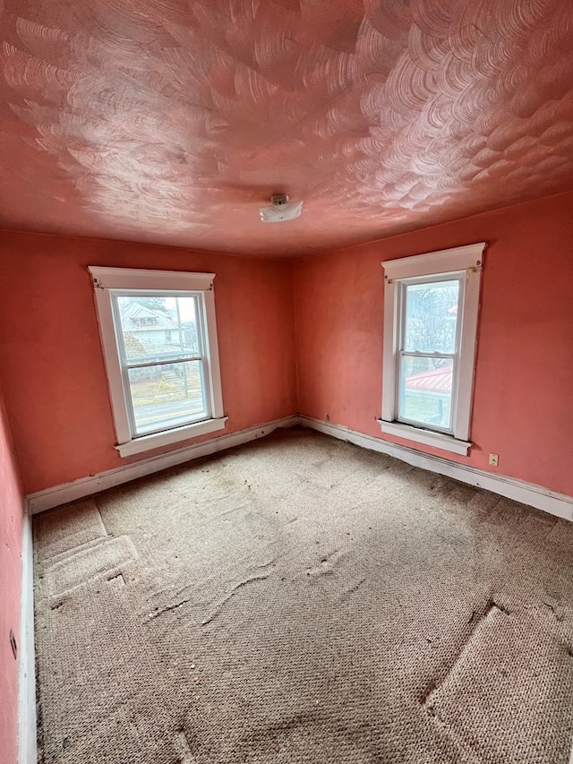 unfurnished room featuring baseboards, a textured ceiling, carpet flooring, and a healthy amount of sunlight