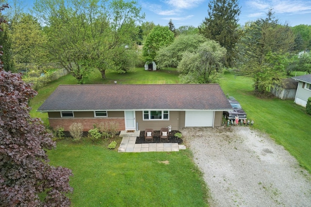 rear view of property with a yard, an attached garage, driveway, and a shingled roof