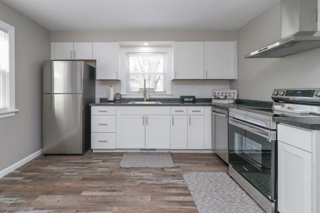 kitchen with appliances with stainless steel finishes, dark hardwood / wood-style floors, white cabinetry, sink, and wall chimney range hood