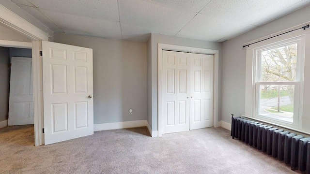 unfurnished bedroom featuring light colored carpet, radiator, multiple windows, and a closet